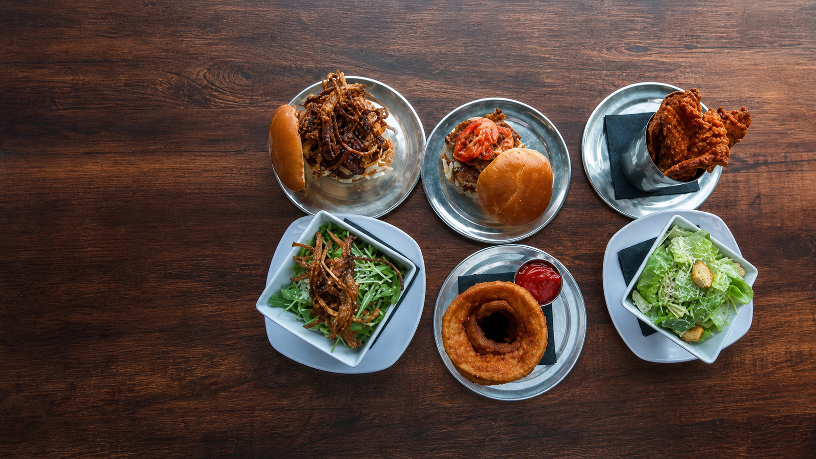 A spread of Grill on Wheel burgers, sides and salads on a wooden table